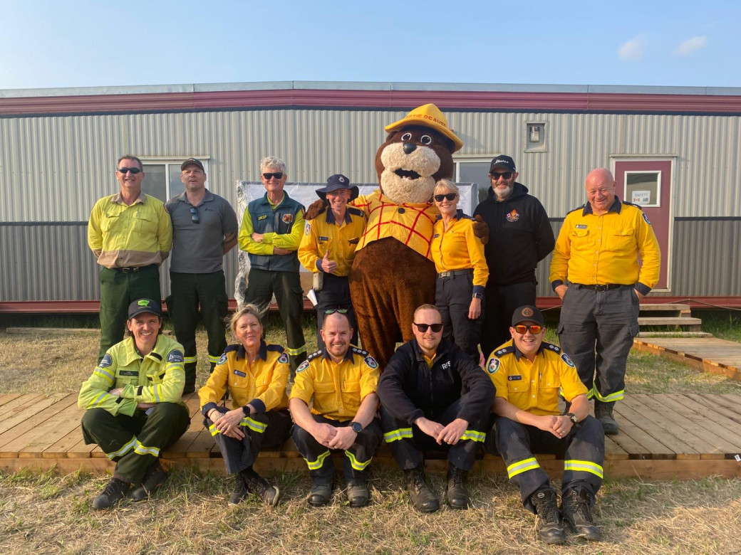 A group of wildland firefighters pose for a photo with a large, anthropomorphic beaver, Bertie Beaver, the Alberta Forestry Mascot
