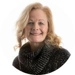 Maggie MacKillop poses for the camera with a big smile wearing a dark sweater.