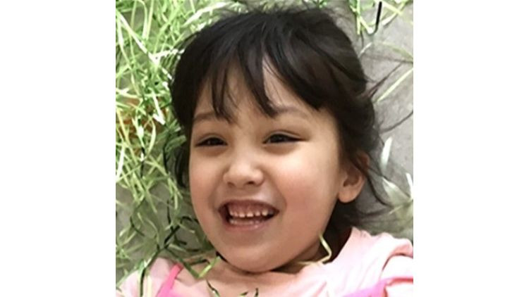 A young child wearing a pink shirt lies outdoors near grass and a paved surface.