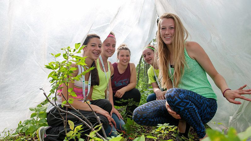 Five teenage girl under a clear tarp with young seedlings