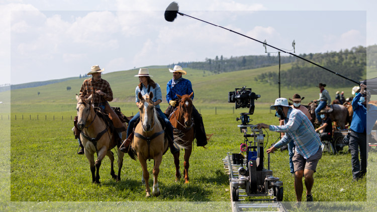 Three people riding on horses while a production crew is filming