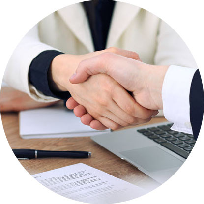 Photo of two people shaking hands over a desk with a pens and papers laying on it.