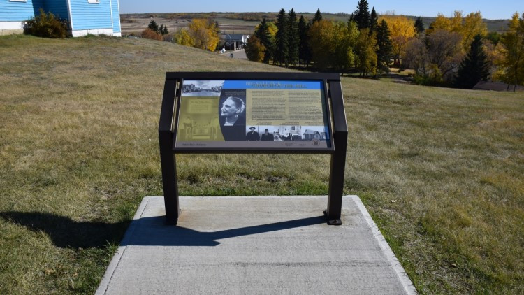 An Alberta heritage marker on a concrete square in a field.
