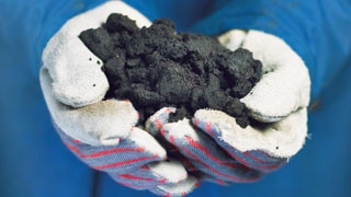 Hands wearing white gloves holding a handful of bitumen