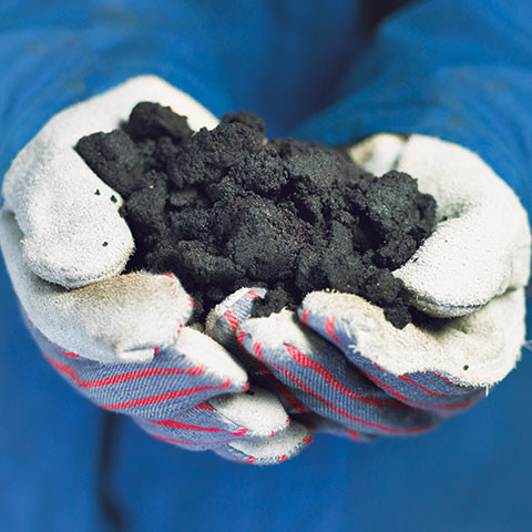 Person wearing a blue outfit and white gloves holding a handful of bitumen