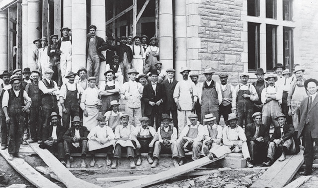 An archival group photo of a construction crew standing in front of the Government House entrance.