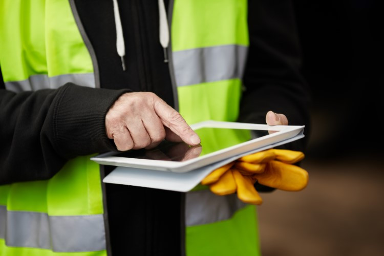 Photo of a worker in a reflective vest looking at an iPad.