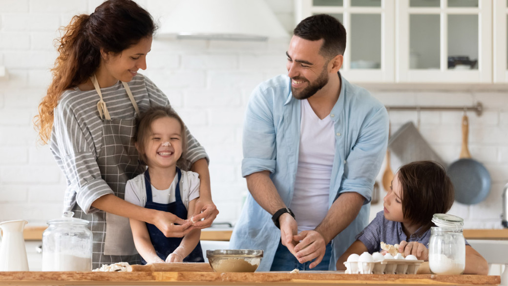 A mom, dad and two young daughters are baking in a kitchen