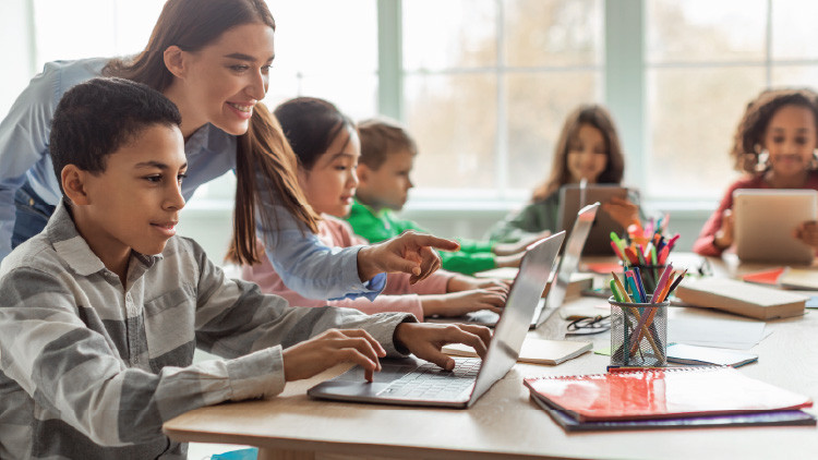 Teacher teaching school kids using laptop in classroom. 