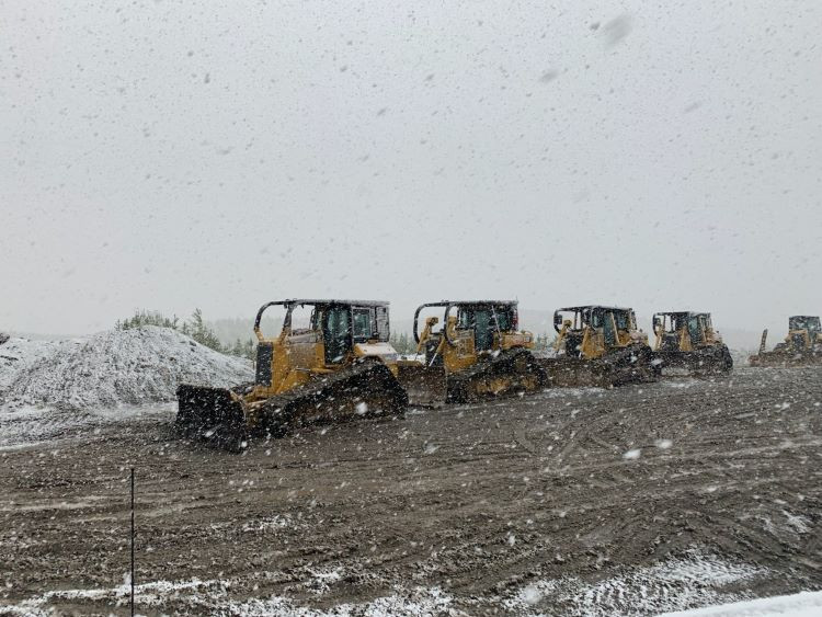 Dozers are parked in a line with snow falling.