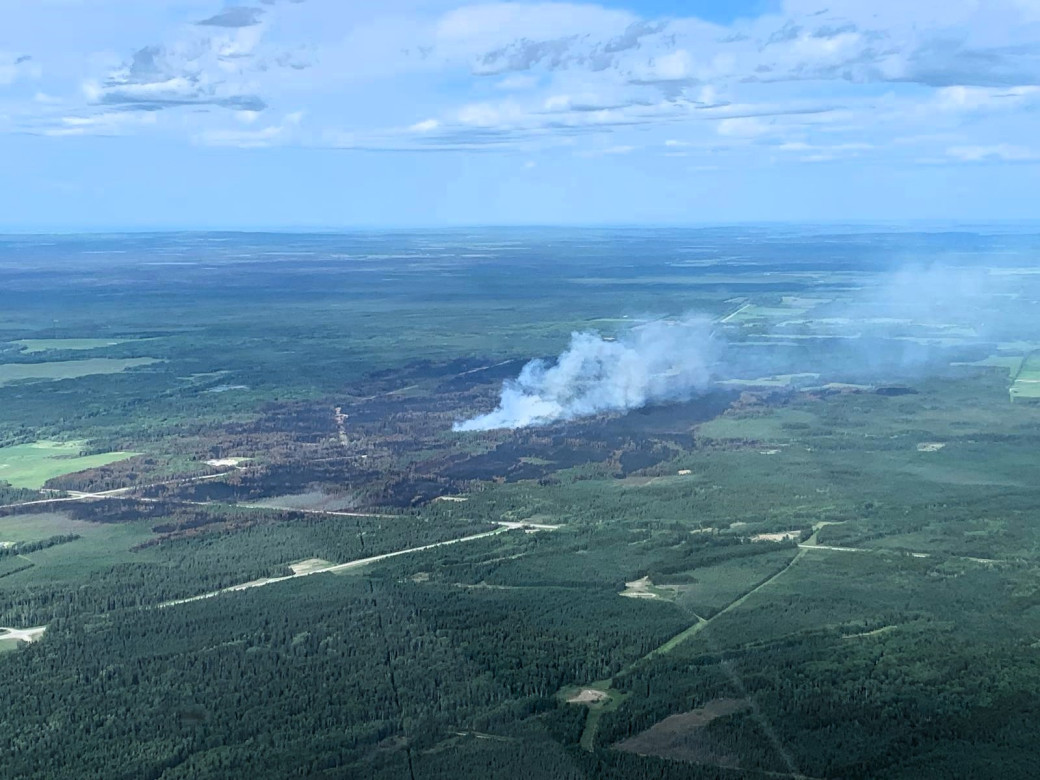Smoke billows from the centre of a burnt tree forest with partial cloudy skies. 