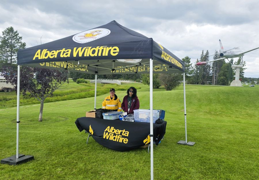 People are standing behind a table and under a black tent with an airplane on a stand in the background.