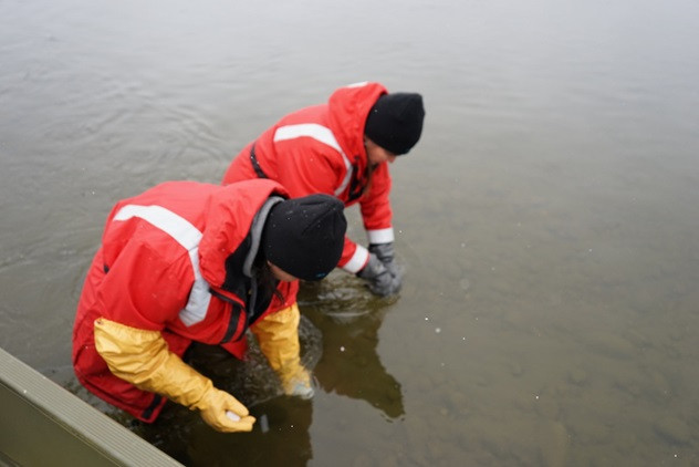 Two individuals in orange safety gear engaged in environmental monitoring fieldwork in an Alberta waterbody.