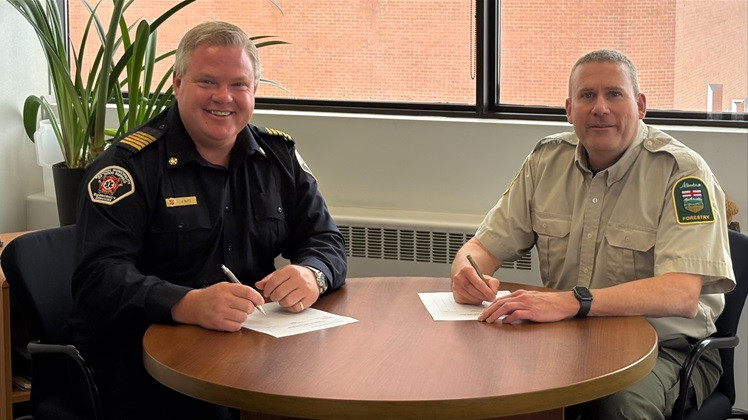 Regional Municipality of Wood Buffalo Fire Chief Jody Butz (left) and Fort McMurray Forest Area Manager (right) seated at a round table.  