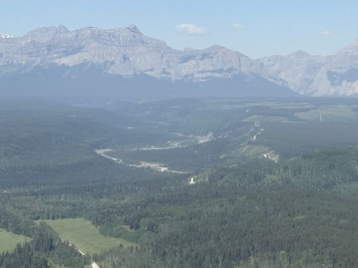 Wide aerial landscape view of forest and mountains. A river flows through the forest. The air is hazy with smoke, but blue skies are still visible. 