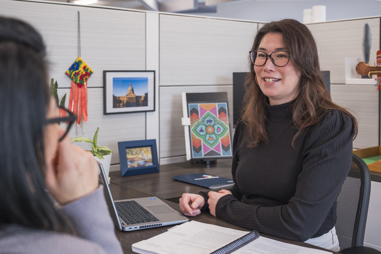 Photo of Indigenous woman at a desk, talking to another person