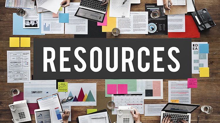 Flat lay view of people at a desk covered in various documents, sticky notes, laptops, phones, water glasses and the word 'Resources' in white text and black background imposed over image