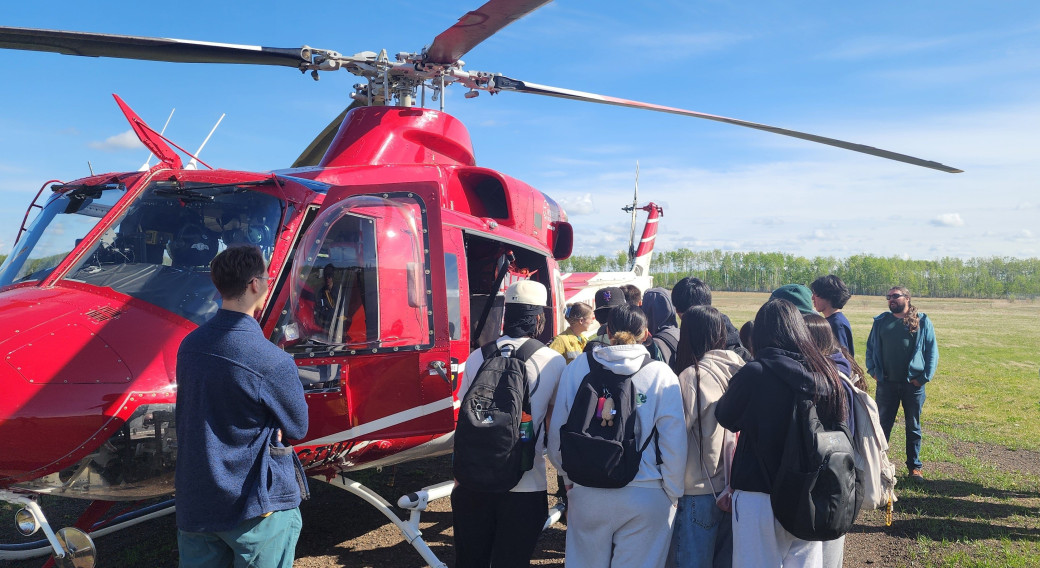 Students at helicopter launch pad with pilot and crew