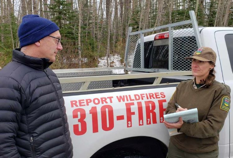 A forest officer fills out a burn permit to a resident infront of an Alberta Wildfire truck that says "report wildfires, call 310-FIRE"