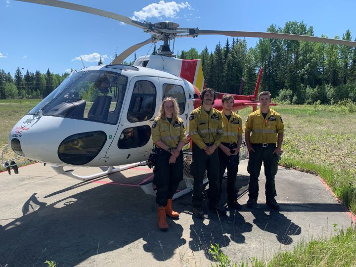 Four wildland firefighters are standing near a helicopter ready to respond to any new wildfires in the Rocky Mountain House Forest Area