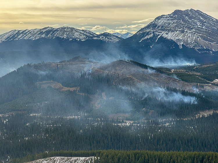 Aerial image shows the lack of snow and a smouldering wildfire on steep terrain in and around a harvest block.
