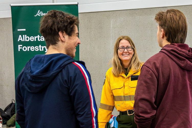 Info officer in yellow shirt speaking with two people at a table. 