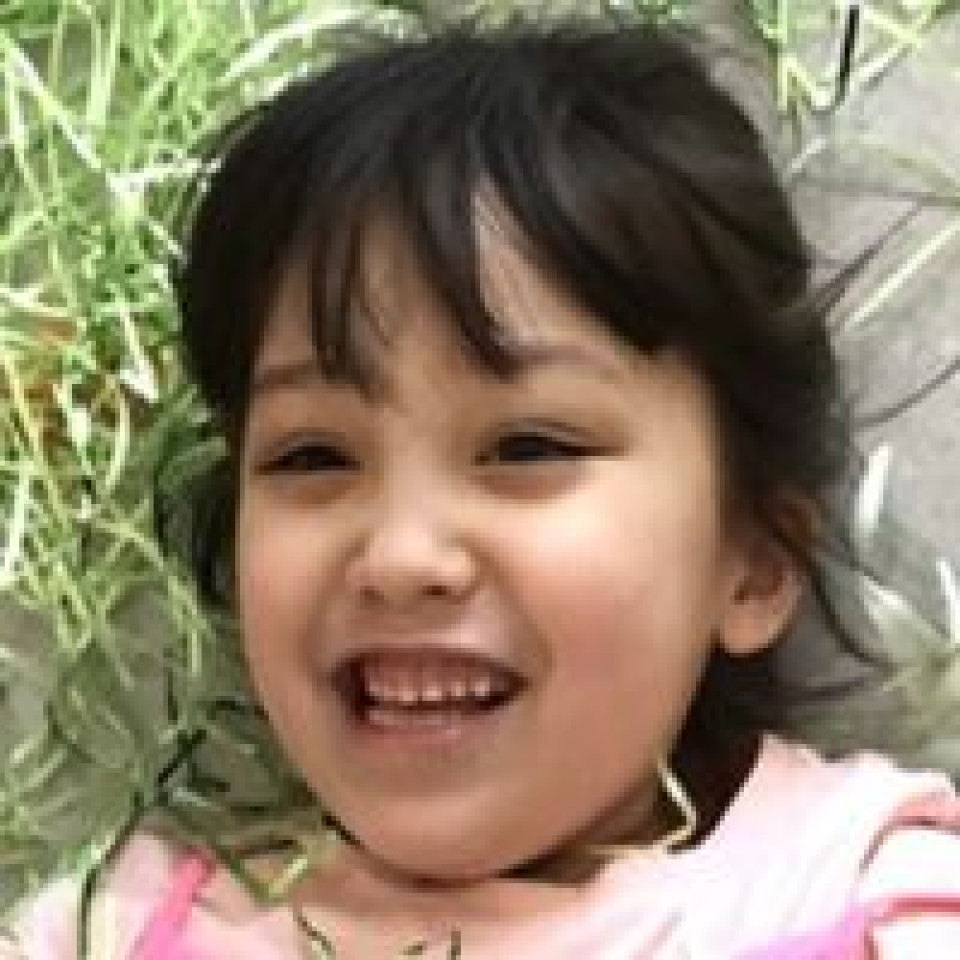 A young child wearing a pink shirt lies outdoors near grass and a paved surface.