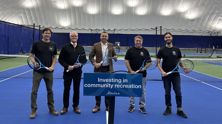 Left to right: Ivan Quintero, Stuart Houston, Minister Andrew Boitchenko, Alex Domnich and Ilan Domnich standing in a pickleball court holding racquets, behind a podium sign with text: Investing in community recreation